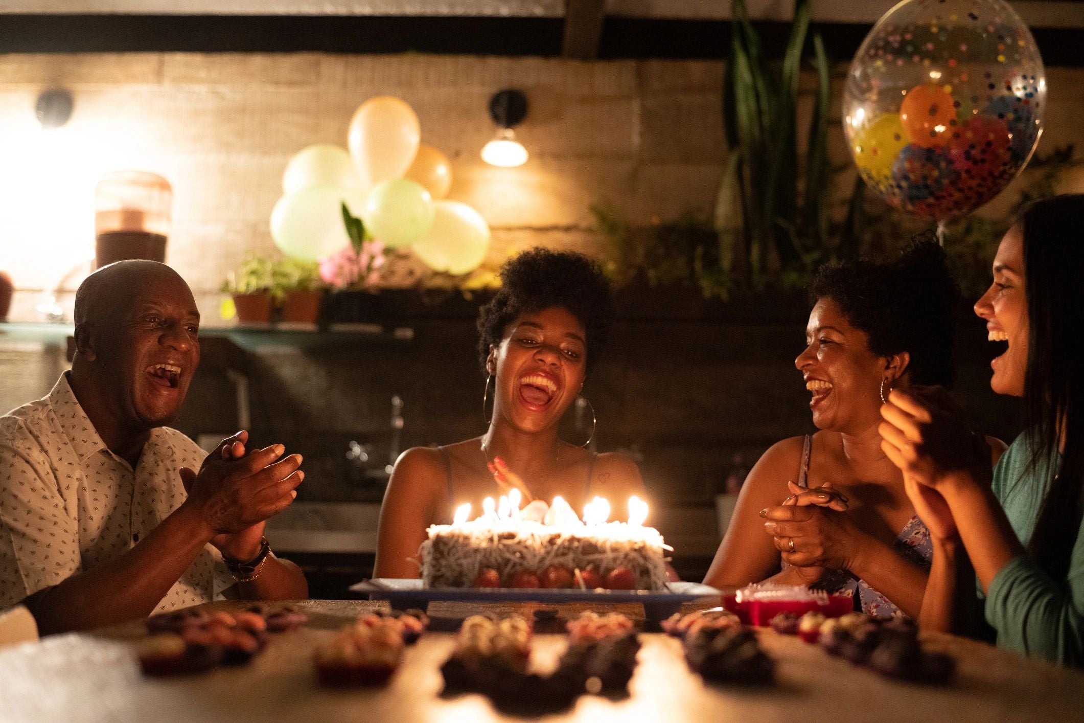 Group of people celebrating a birthday with a cake and candles in a cozy indoor setting.