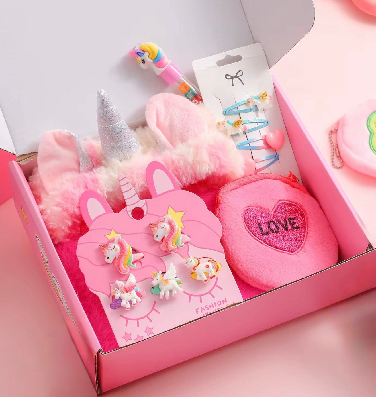 Pink gift box with unicorn-themed earrings, hair accessories, and a heart-shaped pillow.