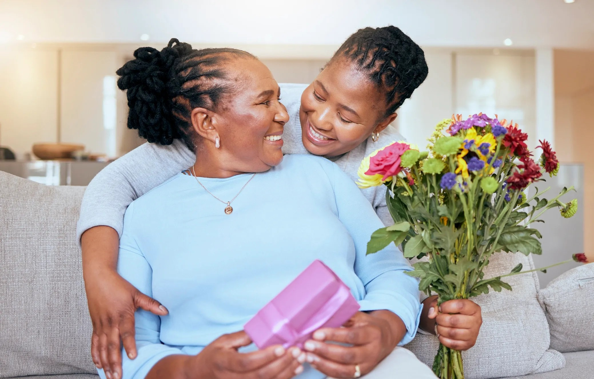 Woman receiving flowers and a gift from a young girl in a home setting.